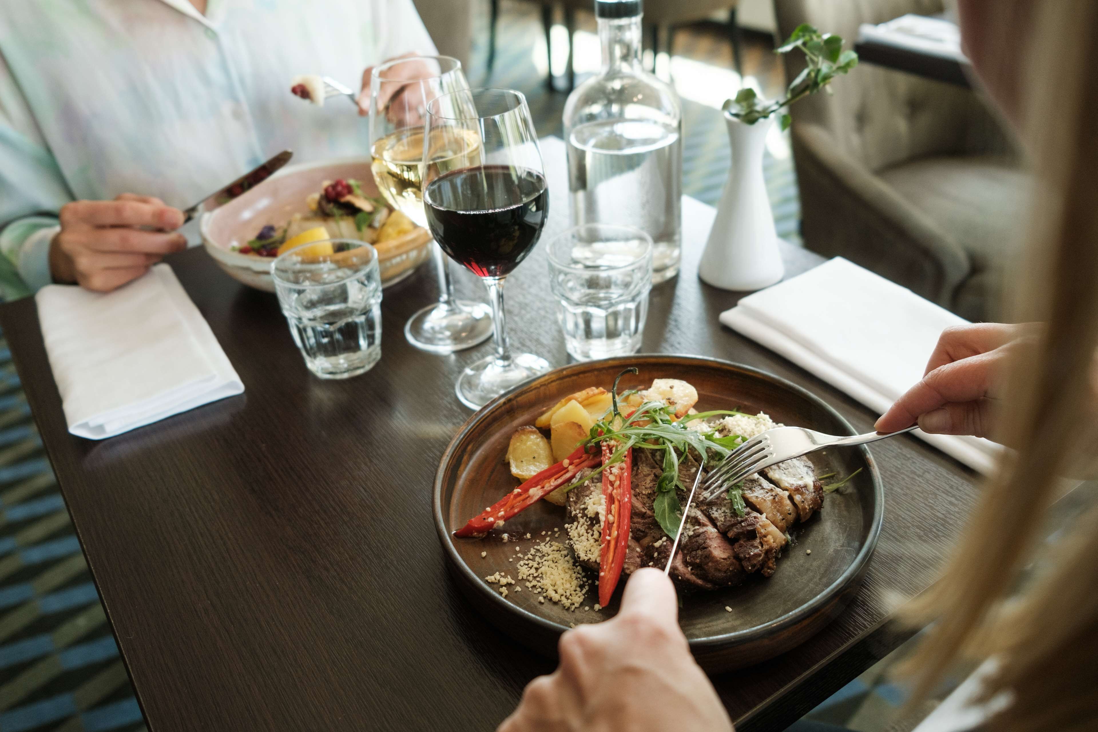 Une table à manger avec une assiette de nourriture, des verres de vin et une bouteille d’eau.