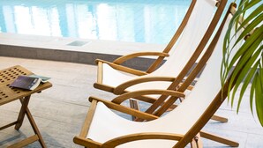 A poolside area with a wooden lounge chair and a table with a book. - Radisson Blu Arlandia Hotel (Arlanda)