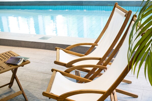 A poolside area with a wooden lounge chair and a table with a book. - Radisson Blu Arlandia Hotel, Stockholm-Arlanda, A Verified Net Zero Hotel (Arlanda)