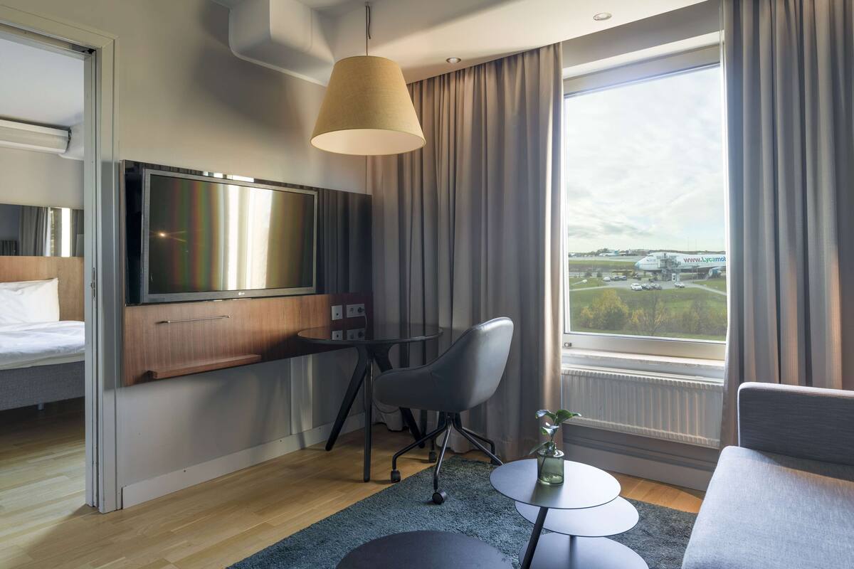Une chambre d’hôtel moderne équipée d’un lit, d’une télévision, d’un bureau et offrant une vue sur un aéroport.