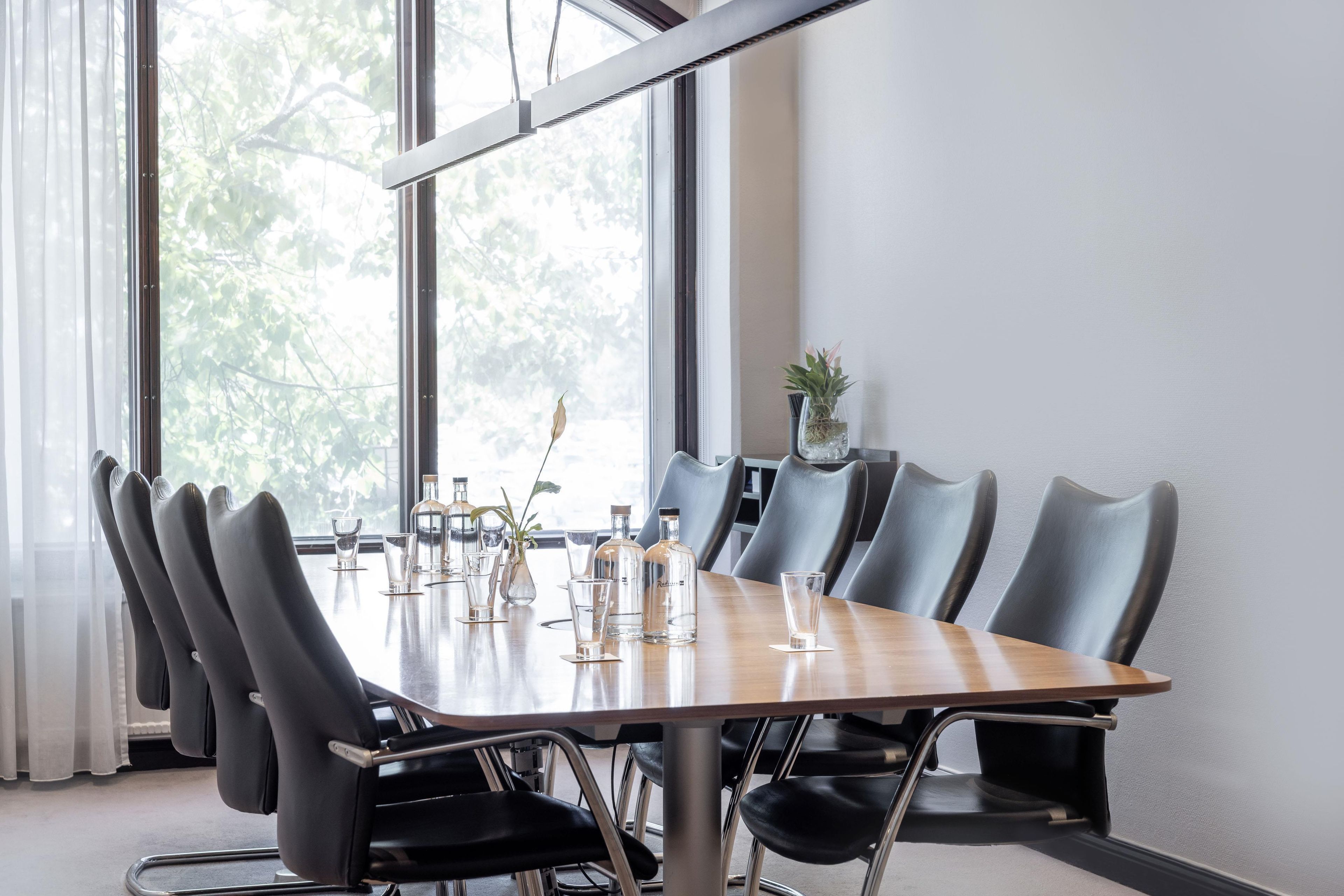 Un salón de conferencias con una mesa larga, varias sillas y una planta en maceta.