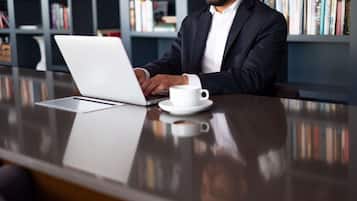 A man sitting at a desk with a laptop and a cup of coffee.