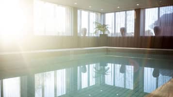 Una amplia piscina cubierta con reflejos nítidos, grandes ventanales con cortinas y una planta en maceta.