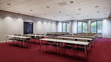 Un salón de conferencias con varias mesas y sillas, amplias ventanas y un suelo cubierto de moqueta roja.