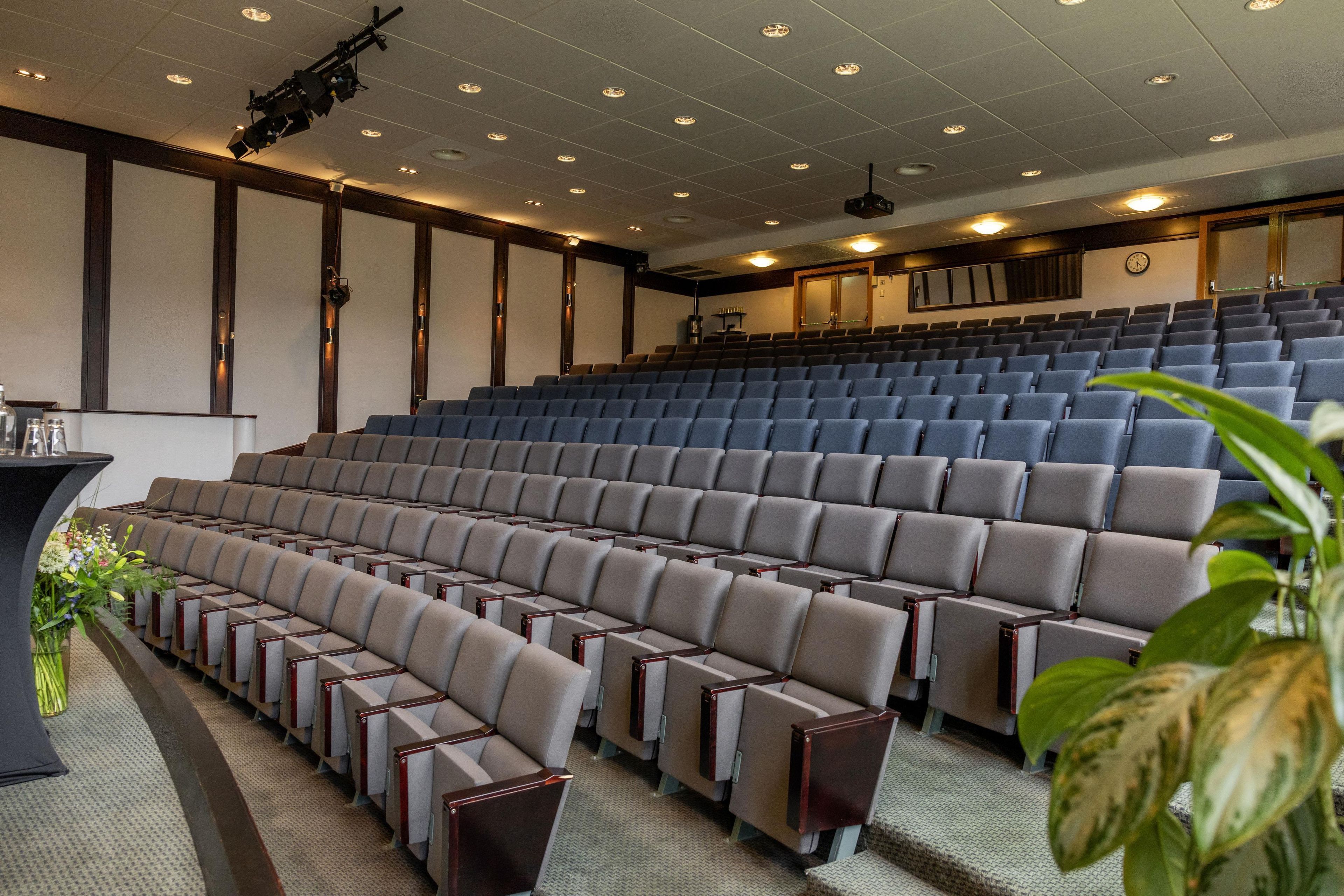 A theater with rows of seats, a stage, and a projector mounted on the ceiling.