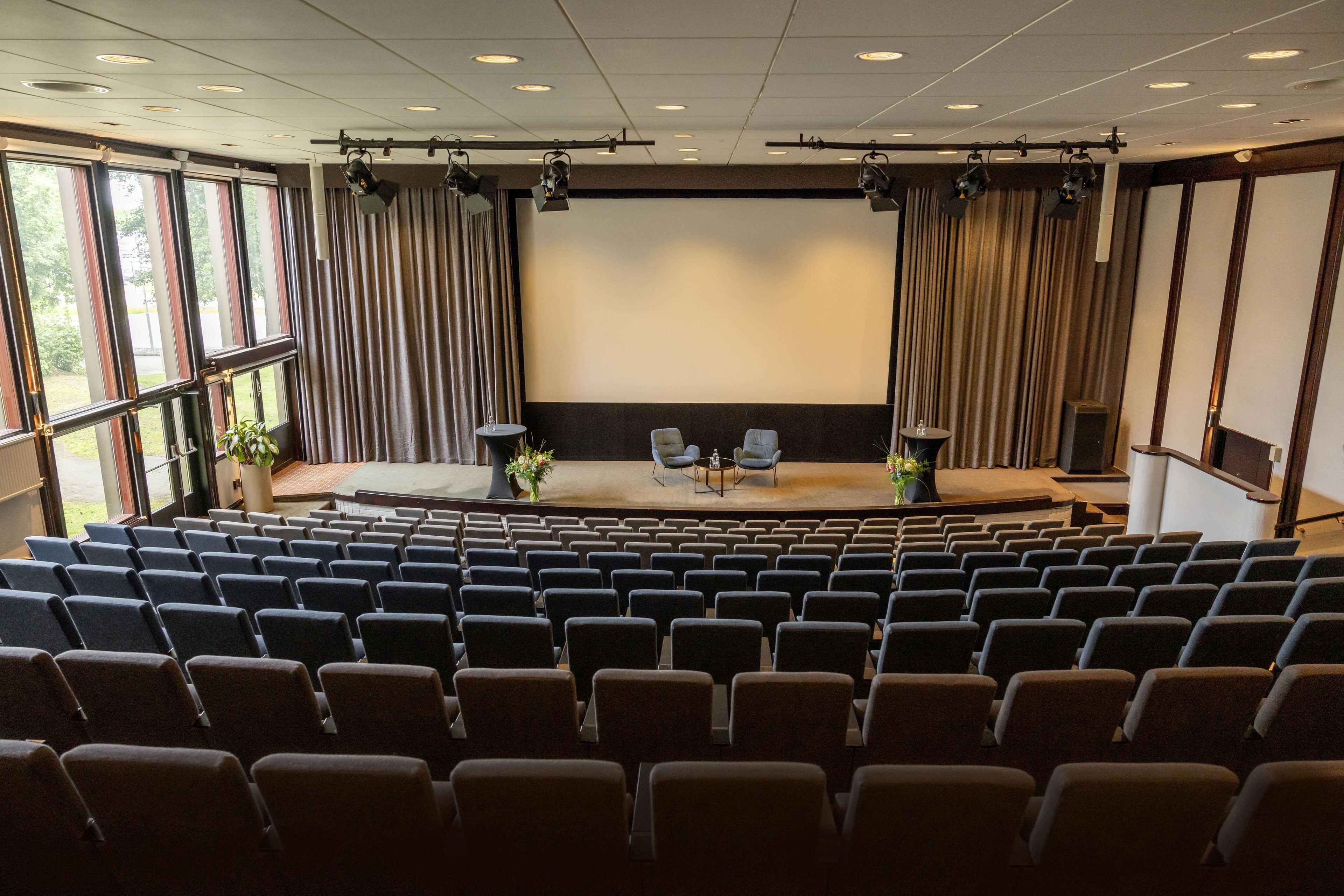 Un salón de conferencias con escenario, asientos y cortinas.