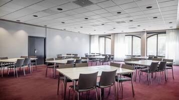 Ein Konferenzraum mit mehreren Tischen und Stühlen, großen Fenstern mit Vorhängen und einer Tür.