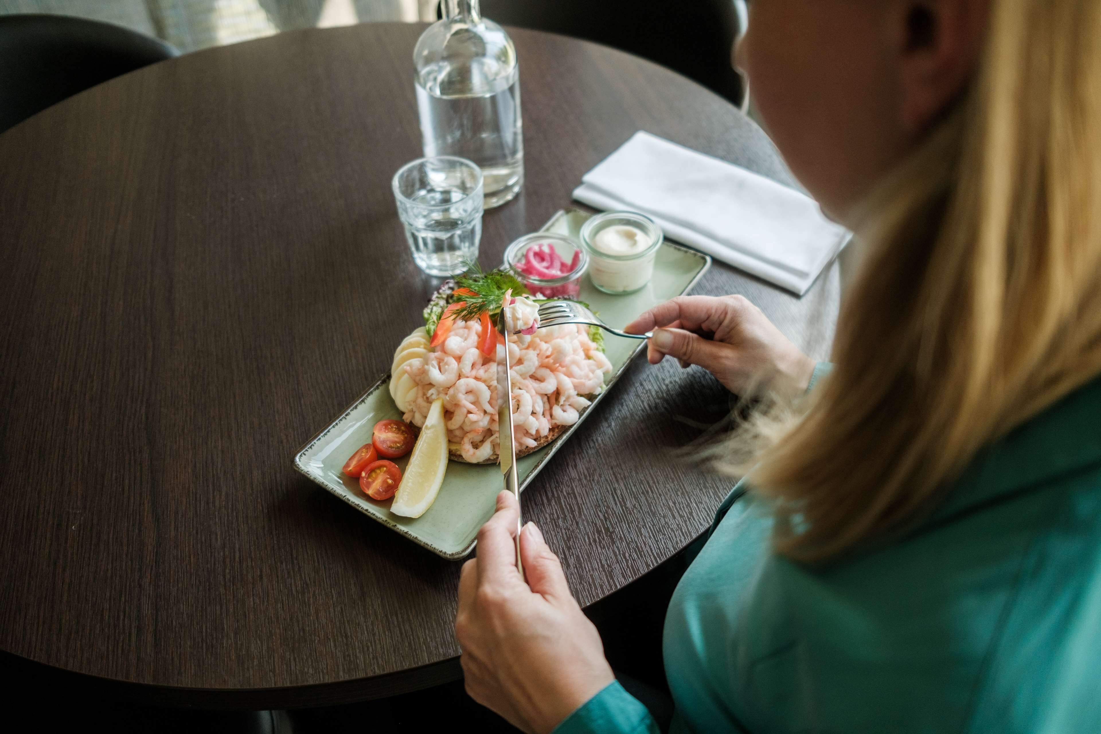 Una persona sta cenando a un tavolo rotondo, con un piatto di cibo, un bicchiere d'acqua e una bottiglia d'acqua.