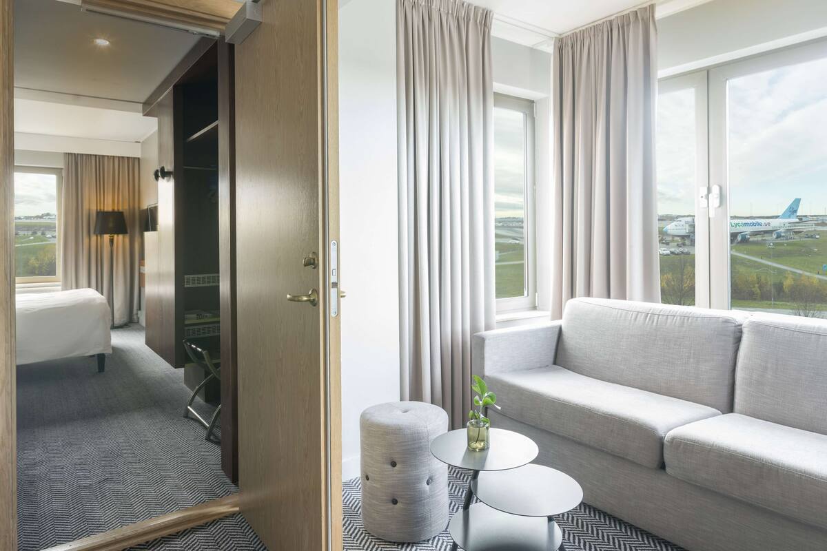 Une chambre d’hôtel avec un lit, un canapé, une petite table et une vue sur un aéroport.