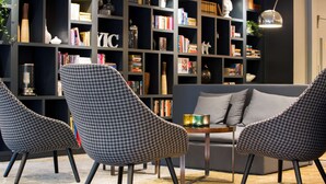 A modern living room with checkered armchairs, a grey sofa, and a bookshelf filled with books and decorative items. - Radisson Blu Arlandia Hotel (Arlanda)