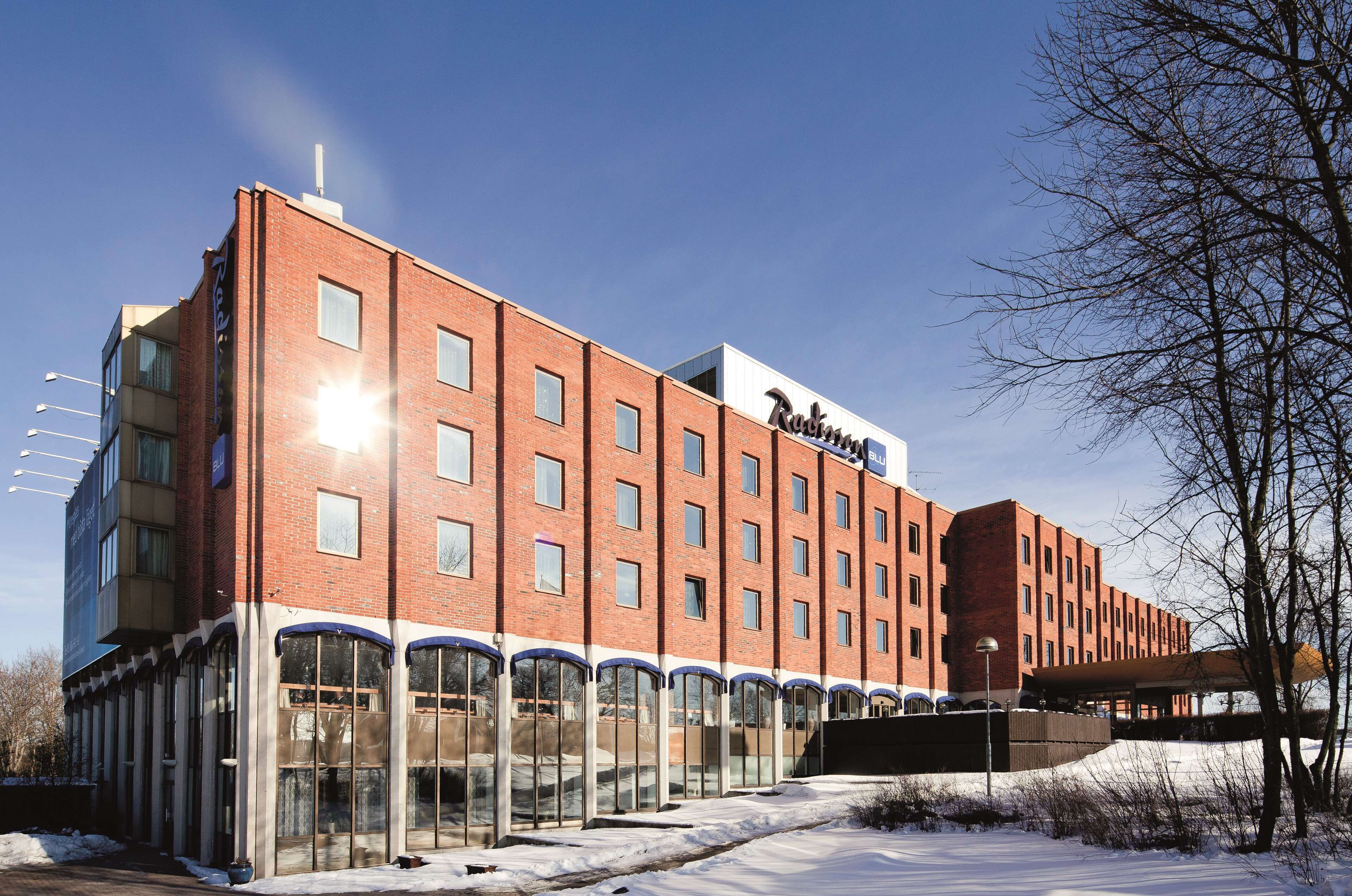Un hôtel en briques rouges au design moderne, avec une enseigne « Radisson » bien visible, de grandes fenêtres en verre et une galerie couverte.