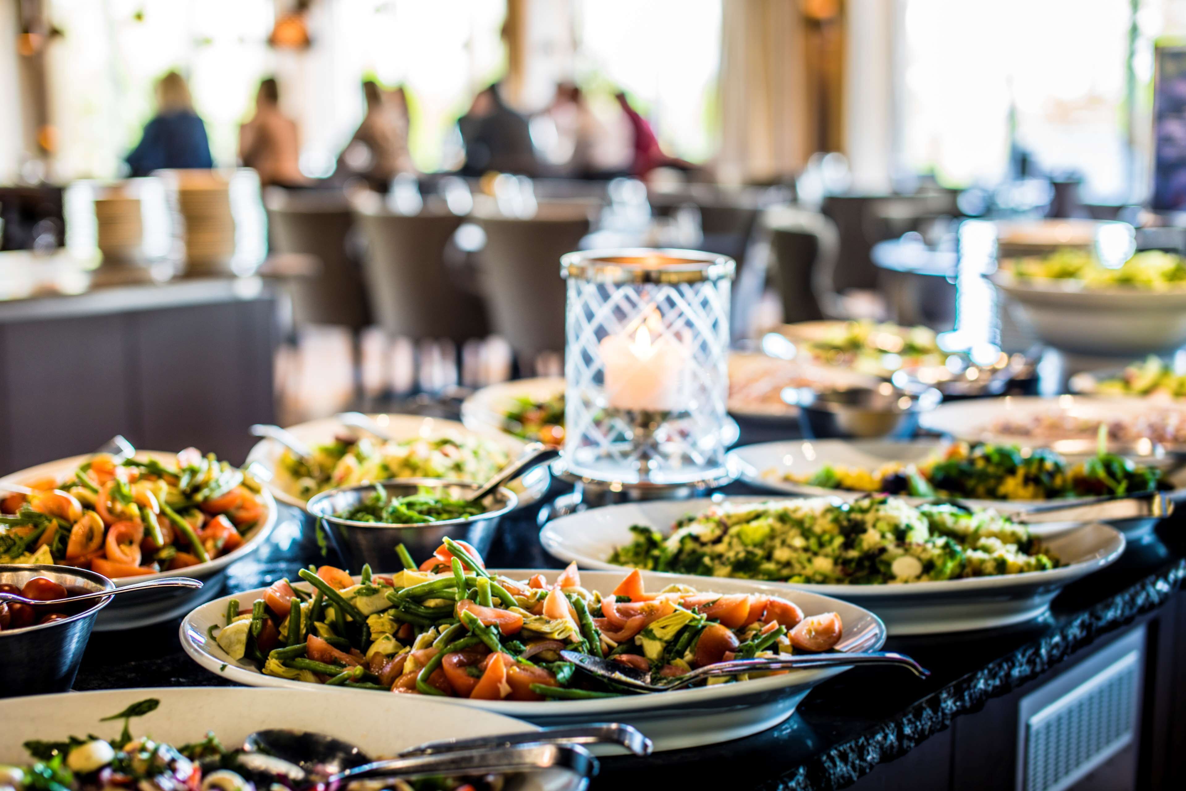 Ein reichhaltiges Buffet mit verschiedenen Speisen, darunter Salate und Gemüse, in einem Essbereich mit Stühlen und Tischen.