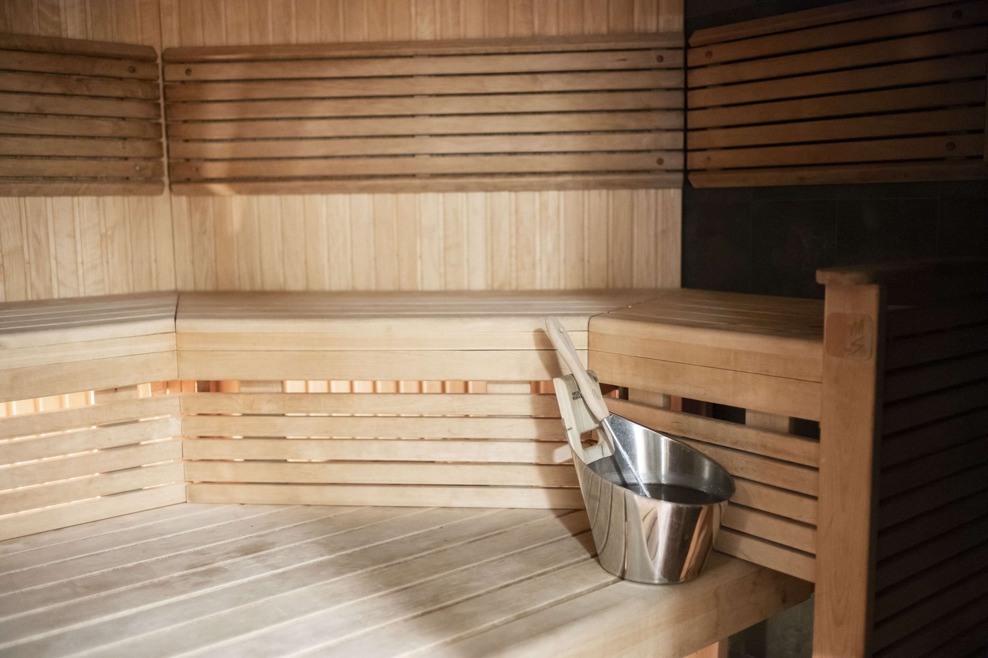 A sauna with wooden benches and a metal bucket.