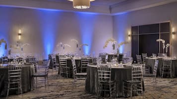 A banquet hall with round tables, clear chairs, and floral centerpieces.