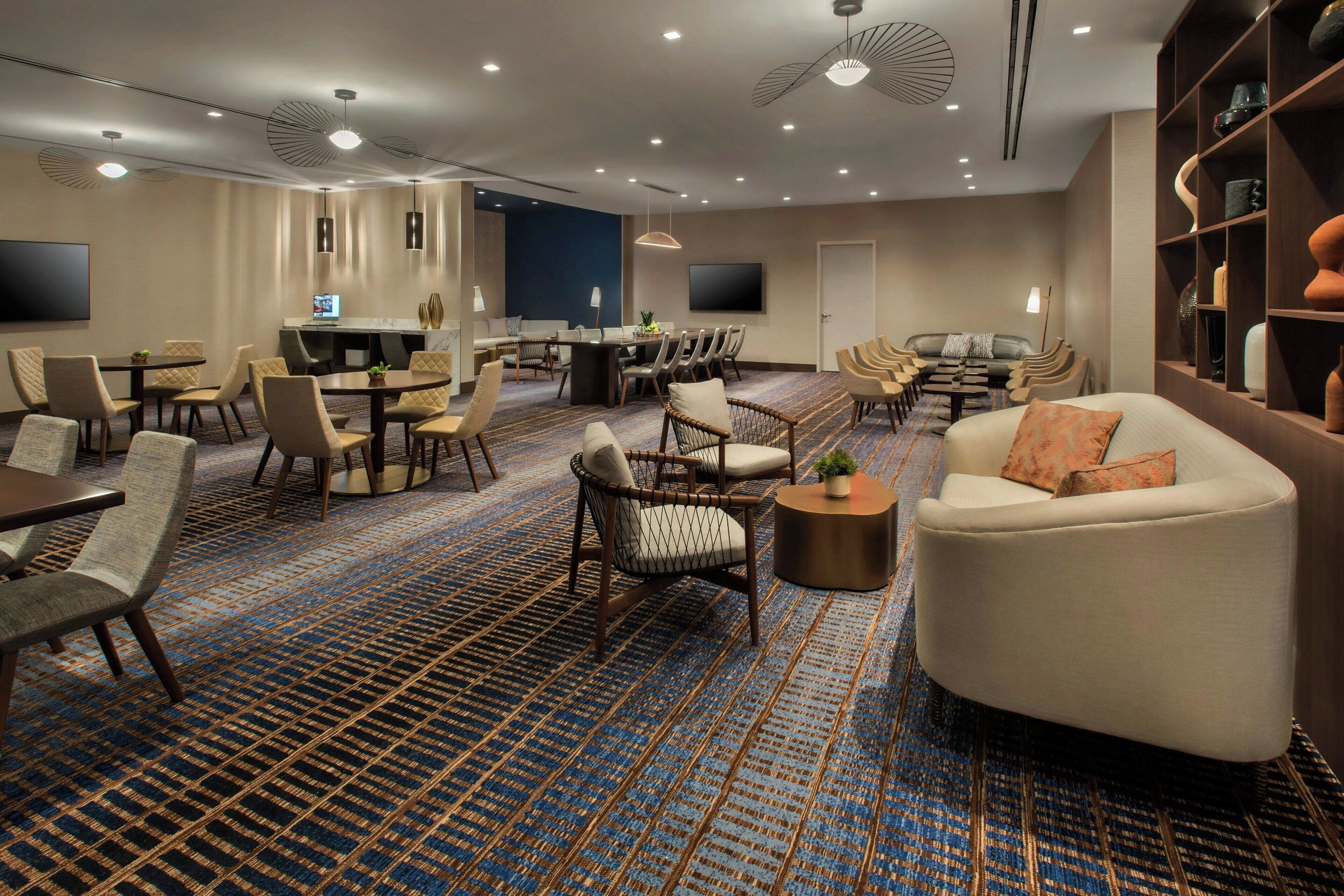 A spacious hotel lobby with a large seating area, a reception desk, and a television screen.