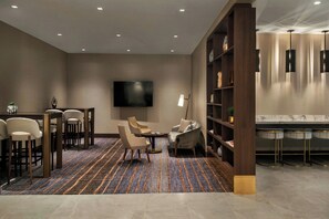 A modern lounge area with a flat-screen TV, comfortable seating, a patterned carpet, and a bar with stools.