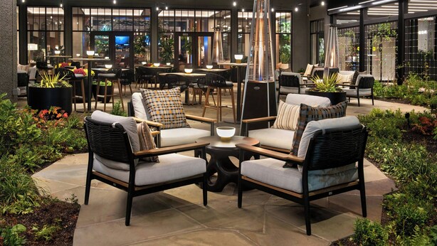 An outdoor seating area with wicker chairs and tables, surrounded by greenery and a modern lamp structure. - Westchester Marriott (Tarrytown)