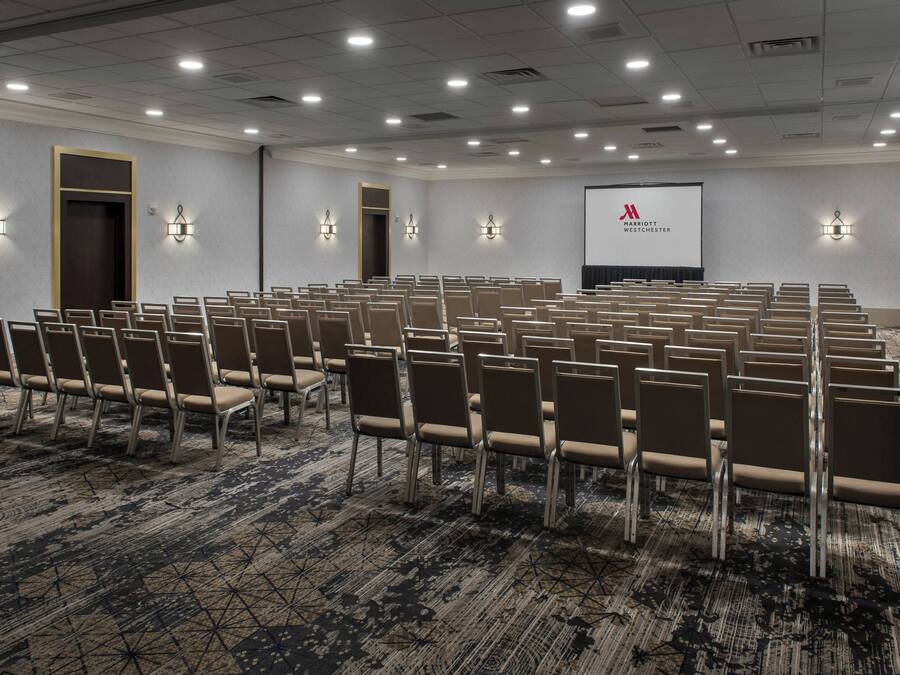 A conference room with rows of chairs, a projector screen, and wall-mounted lights.