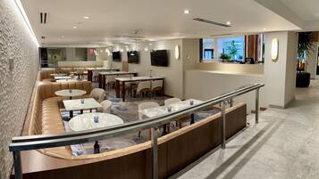 A modern hotel lobby with leather seating, marble tables, and a staircase with a glass railing.