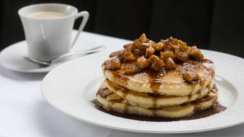 Una pila de panqueques con salsa de caramelo y una taza de café sobre un plato blanco.