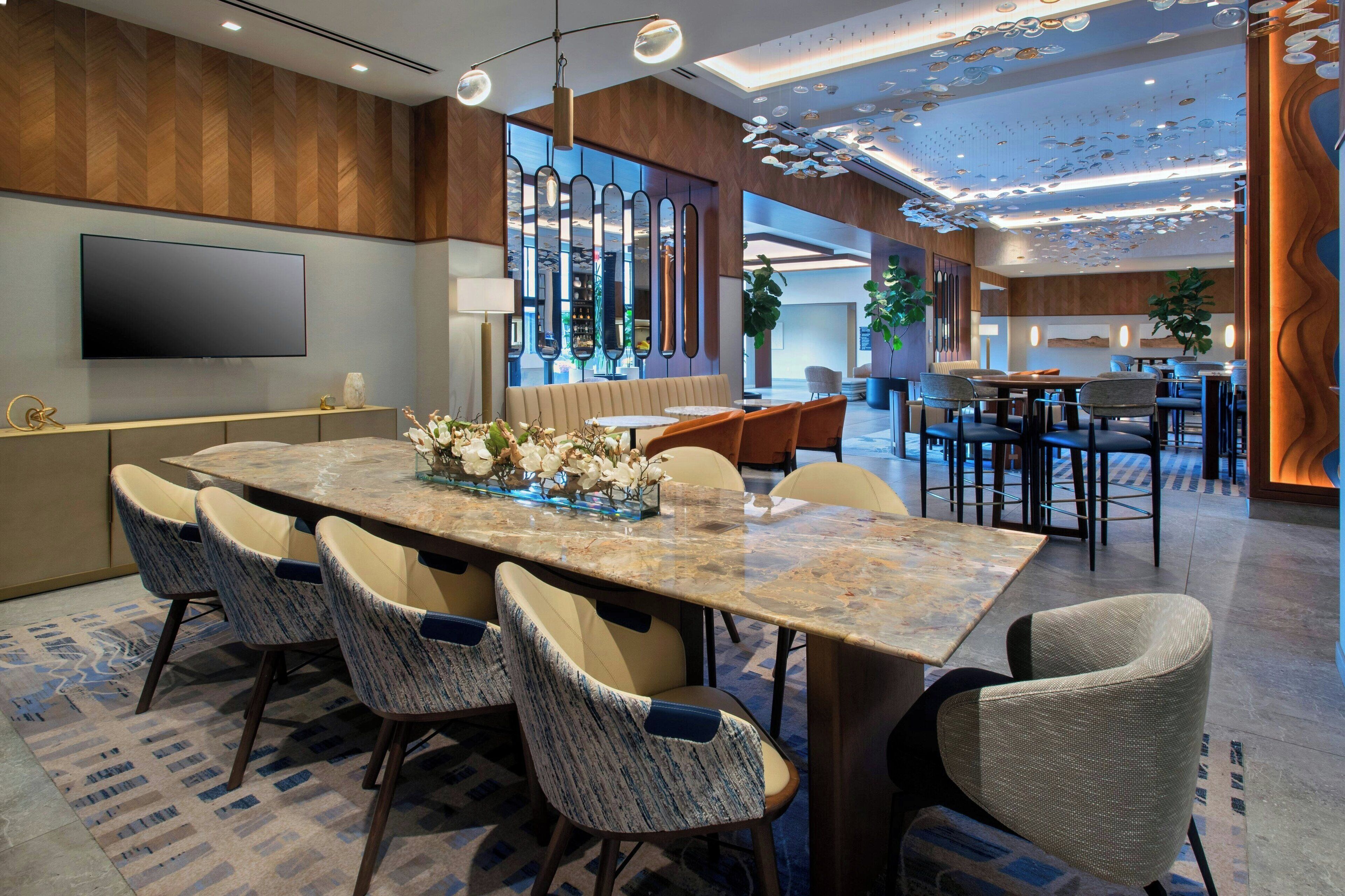 A modern hotel lobby with a large marble reception desk, comfortable seating, a flat-screen TV, and decorative ceiling elements.