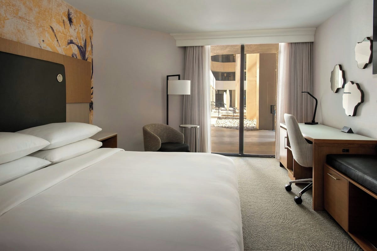A hotel room with a large bed, a desk, a chair, and a view of the outdoor area.
