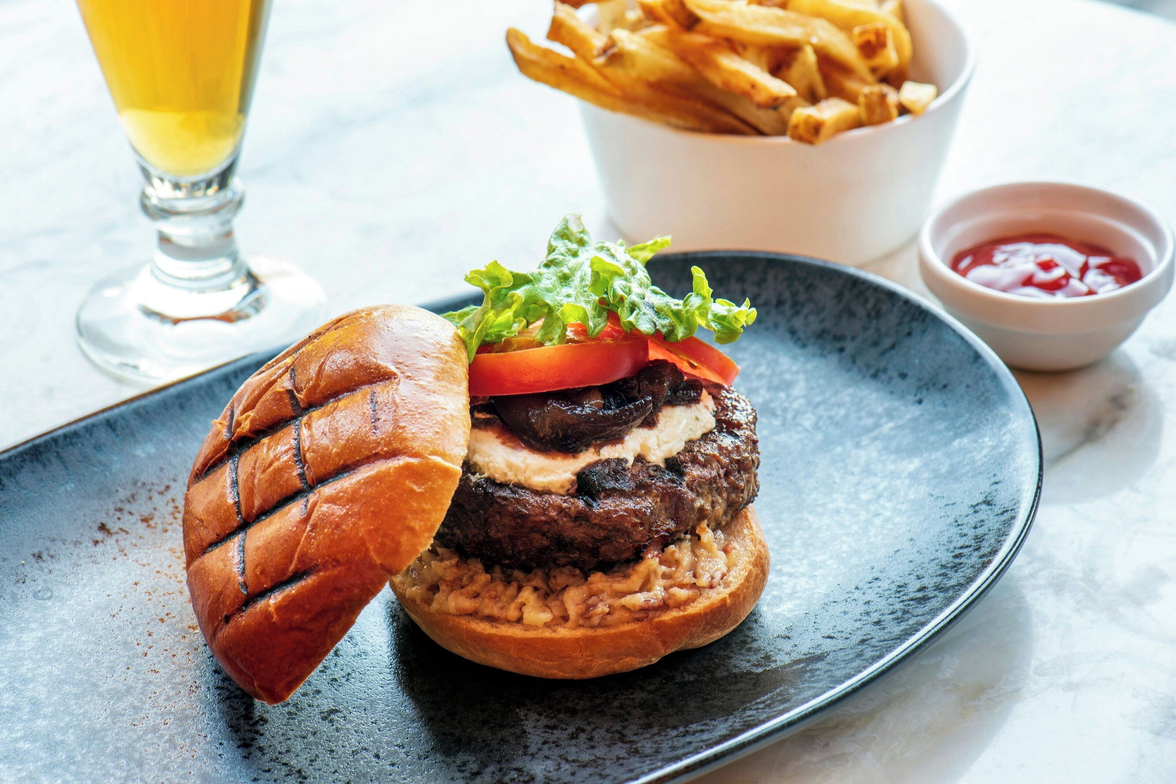 A burger with lettuce, tomato, and a bun on a plate, accompanied by fries and ketchup in a bowl.