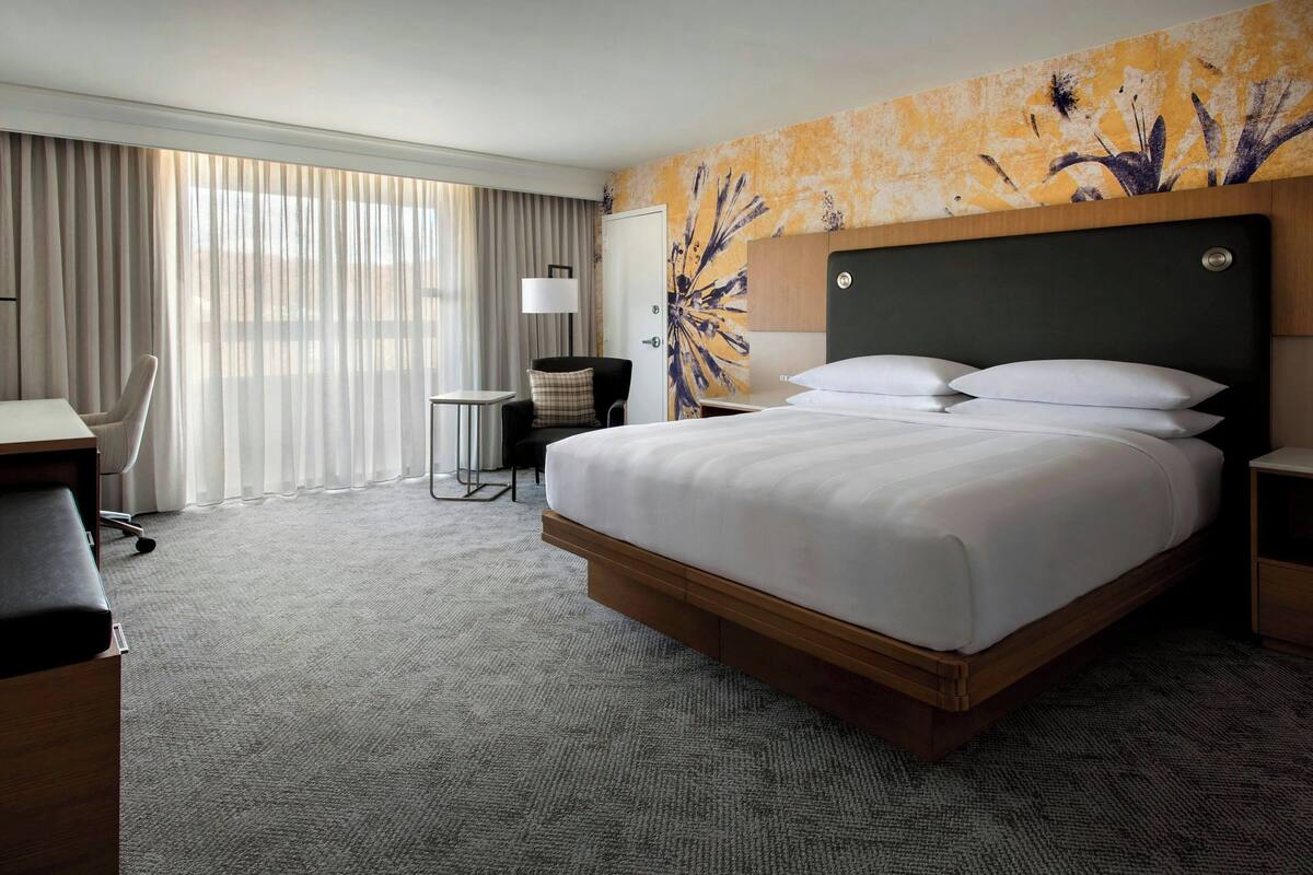 A hotel room with a large bed, a desk, a chair, and a view of the outdoors through the window.