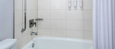 A bathroom with a bathtub, a toilet, and a handrail. There are three bottles of shampoo and conditioner on the wall.