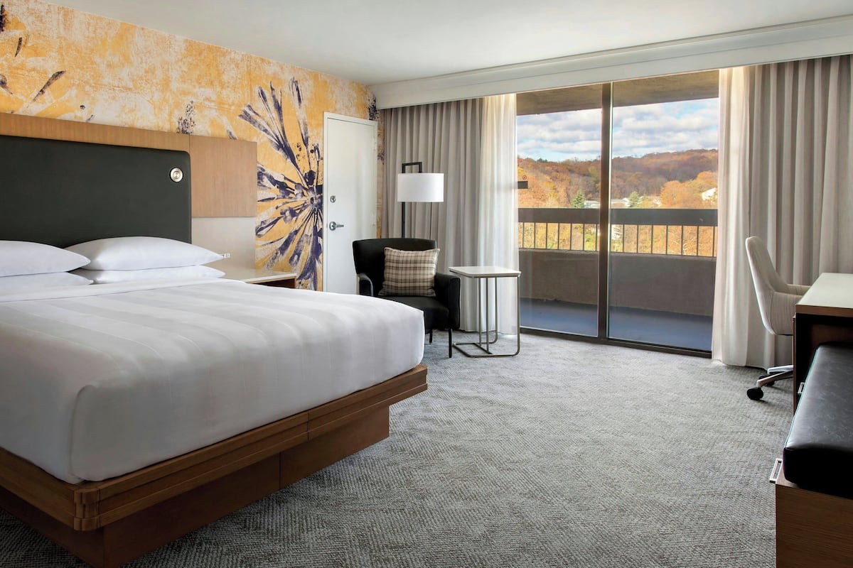 A hotel room with a large bed, a desk, a chair, and a view of the outdoors.