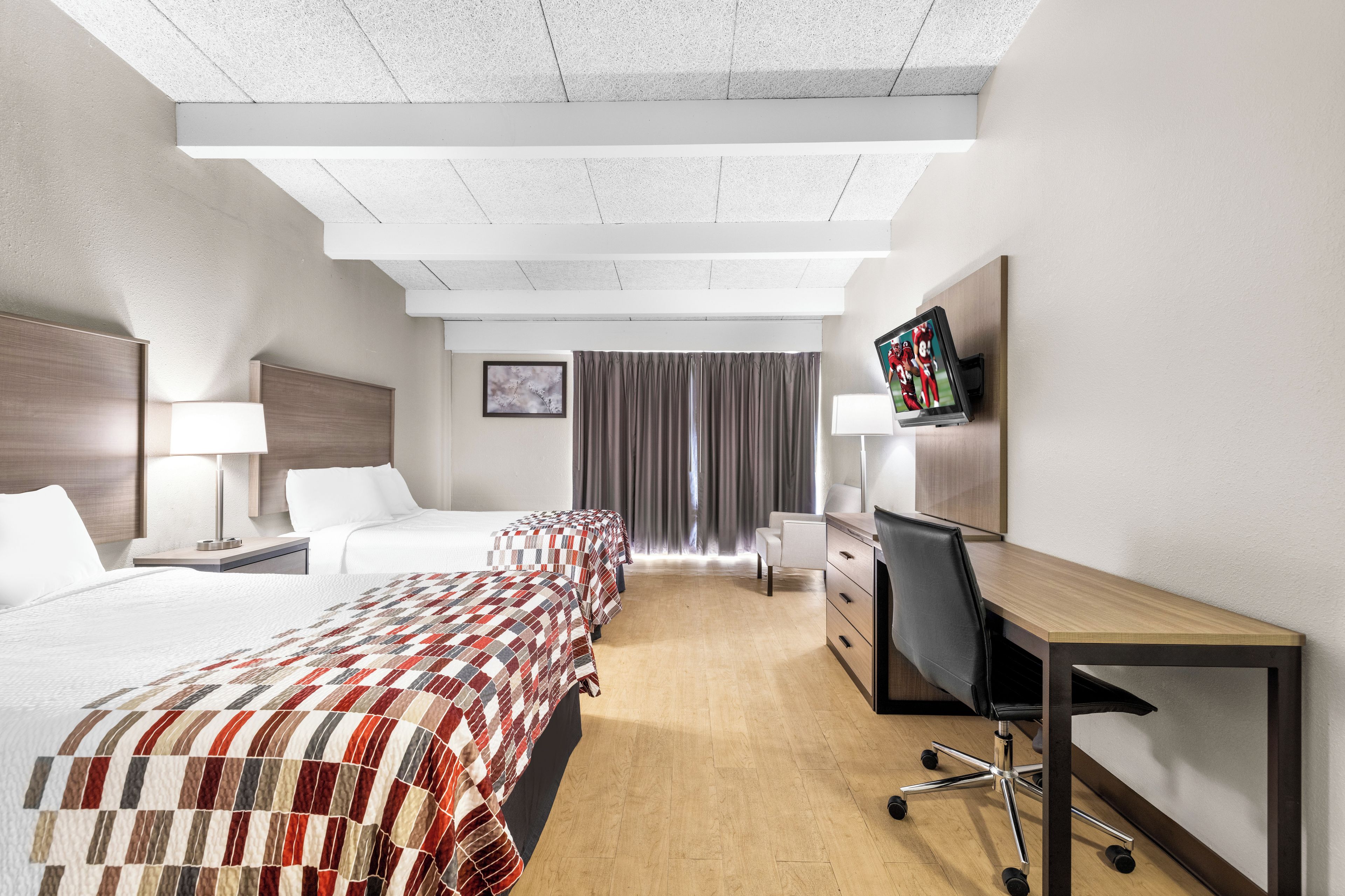 Habitación de hotel con una cama grande, un escritorio con una silla, un televisor y una ventana con cortinas.