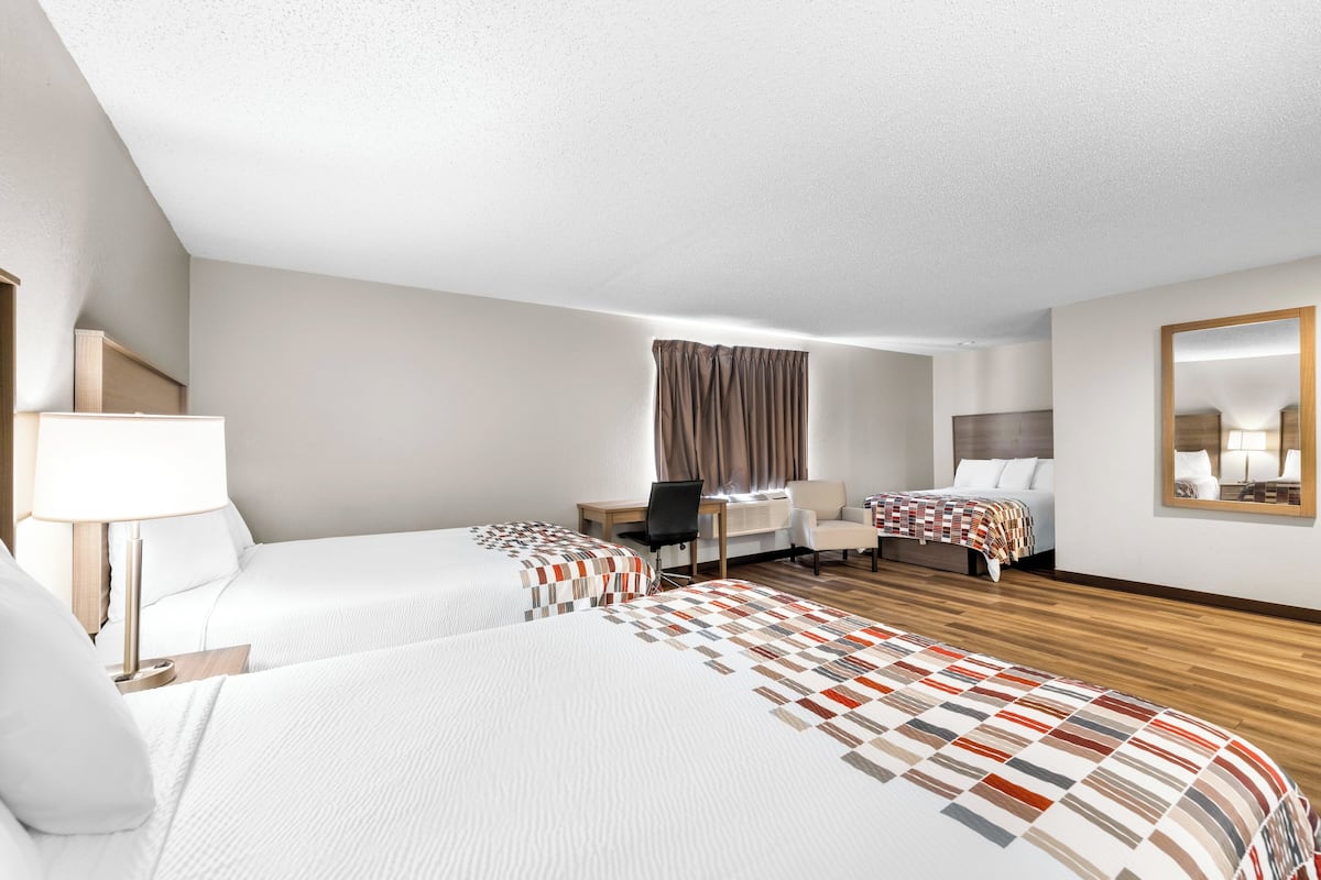 Habitación de hotel con dos camas, un escritorio, una silla, un sofá y un espejo grande.