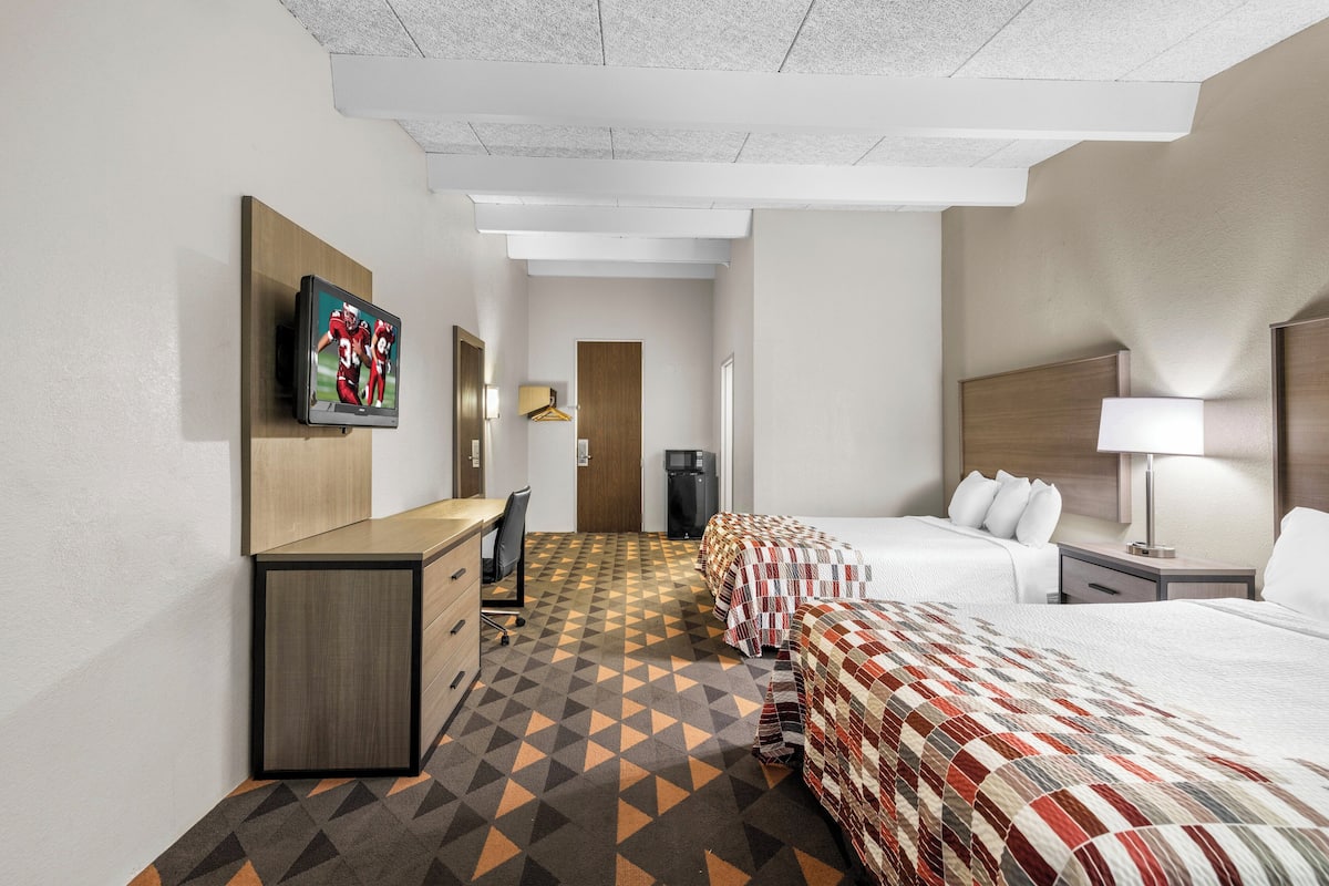 Habitación de hotel con cama, escritorio, silla, televisor montado en la pared y piso estampado.