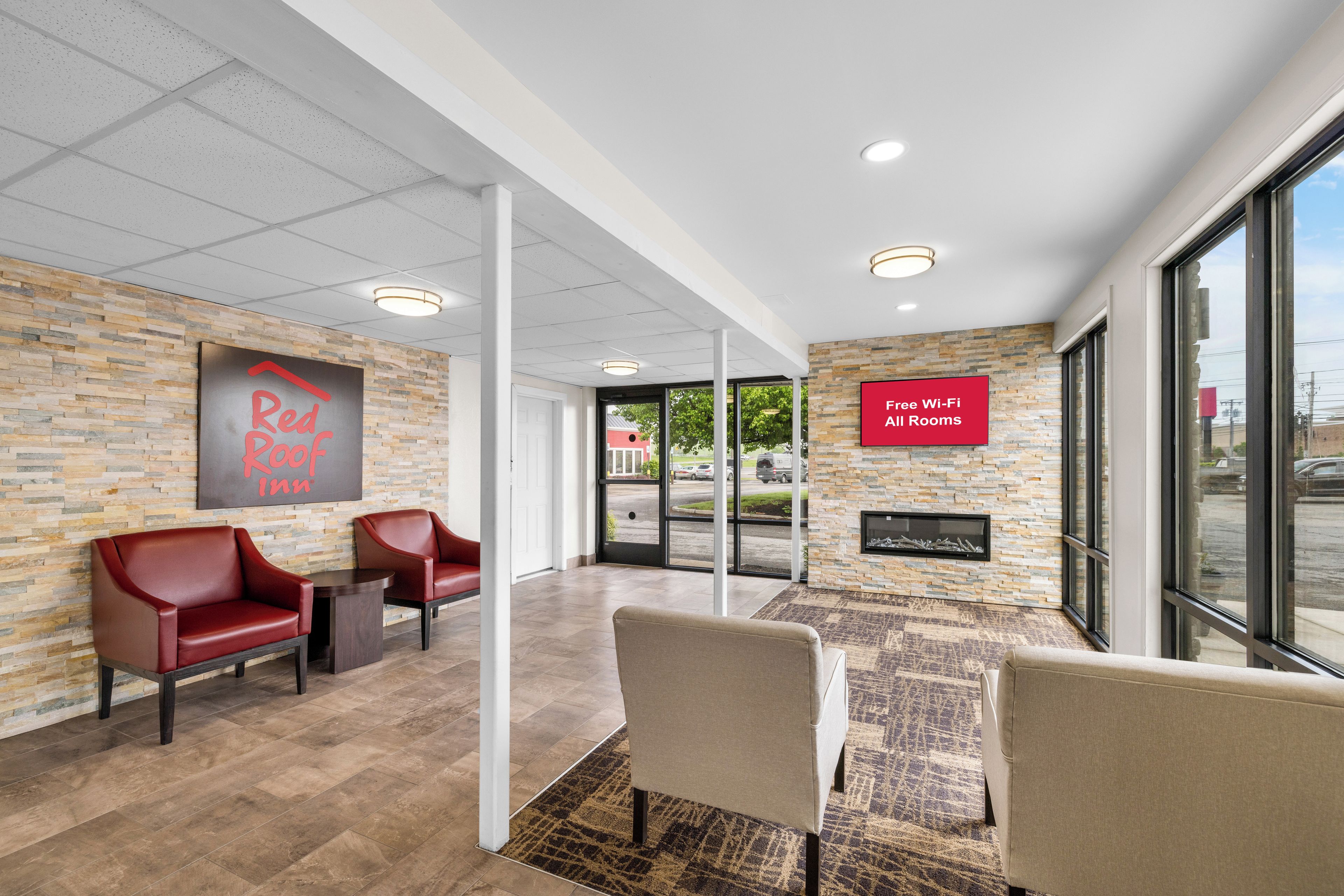 A Red Roof Inn lobby with a stone wall, leather chairs, a fireplace, and a sign indicating all rooms have Wi-Fi.