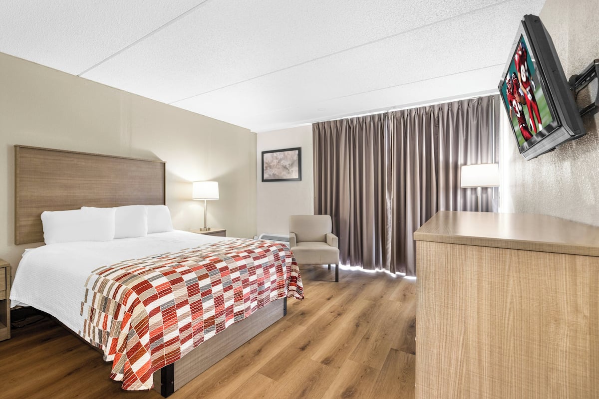 Habitación de hotel con cama, escritorio, silla, televisor y ventana con cortinas.