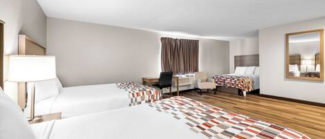 A hotel room with two beds, a desk, a chair, a mirror, and a window with curtains.