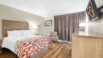 A hotel room with a bed, a desk, a chair, a TV, and curtains.