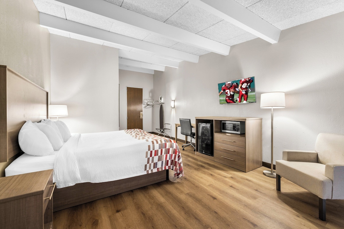 A hotel room with a bed, bedside table, desk, chair, wardrobe, and a flat-screen TV.