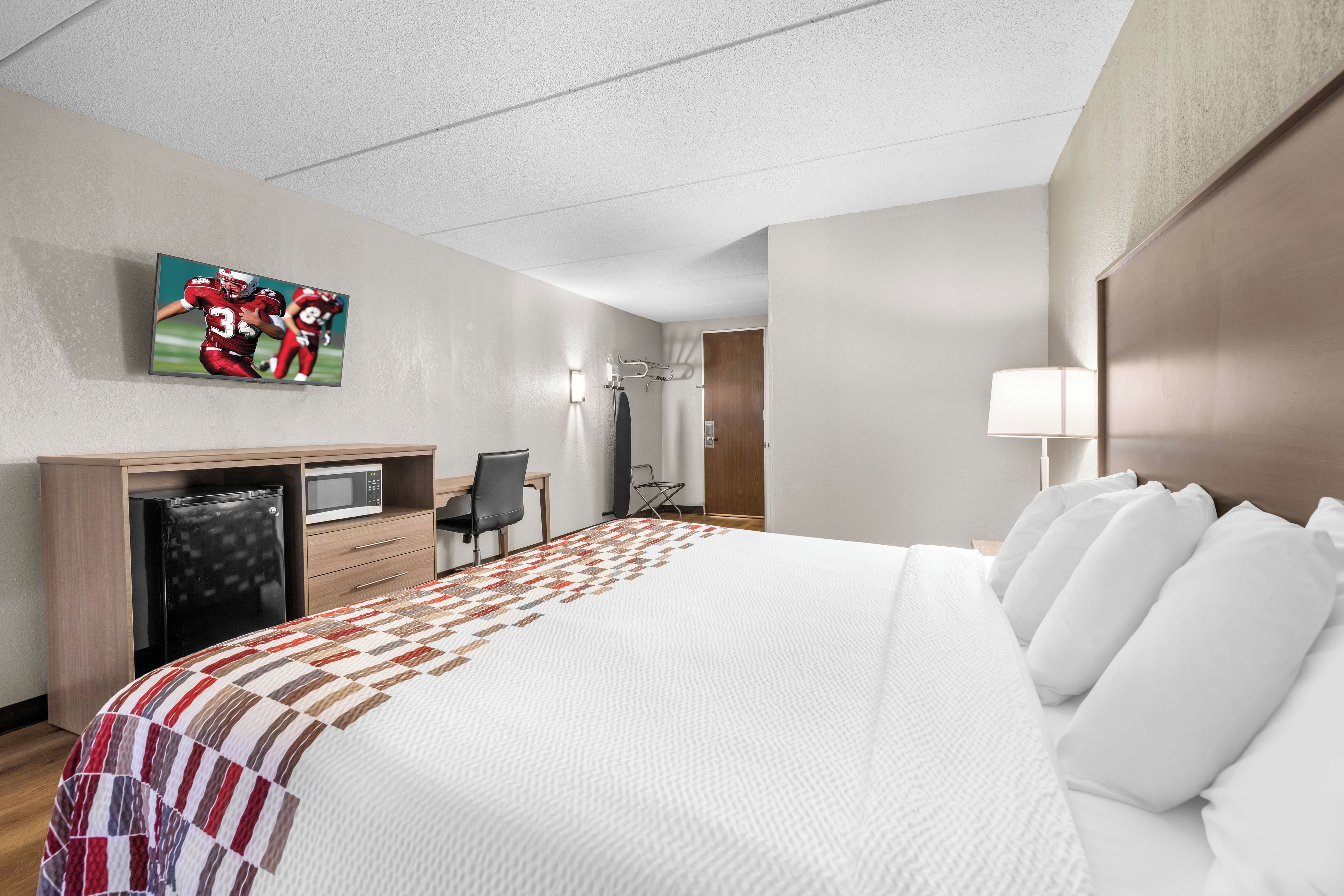 Habitación de hotel con cama, escritorio con computadora, televisor montado en la pared y zona de ducha.