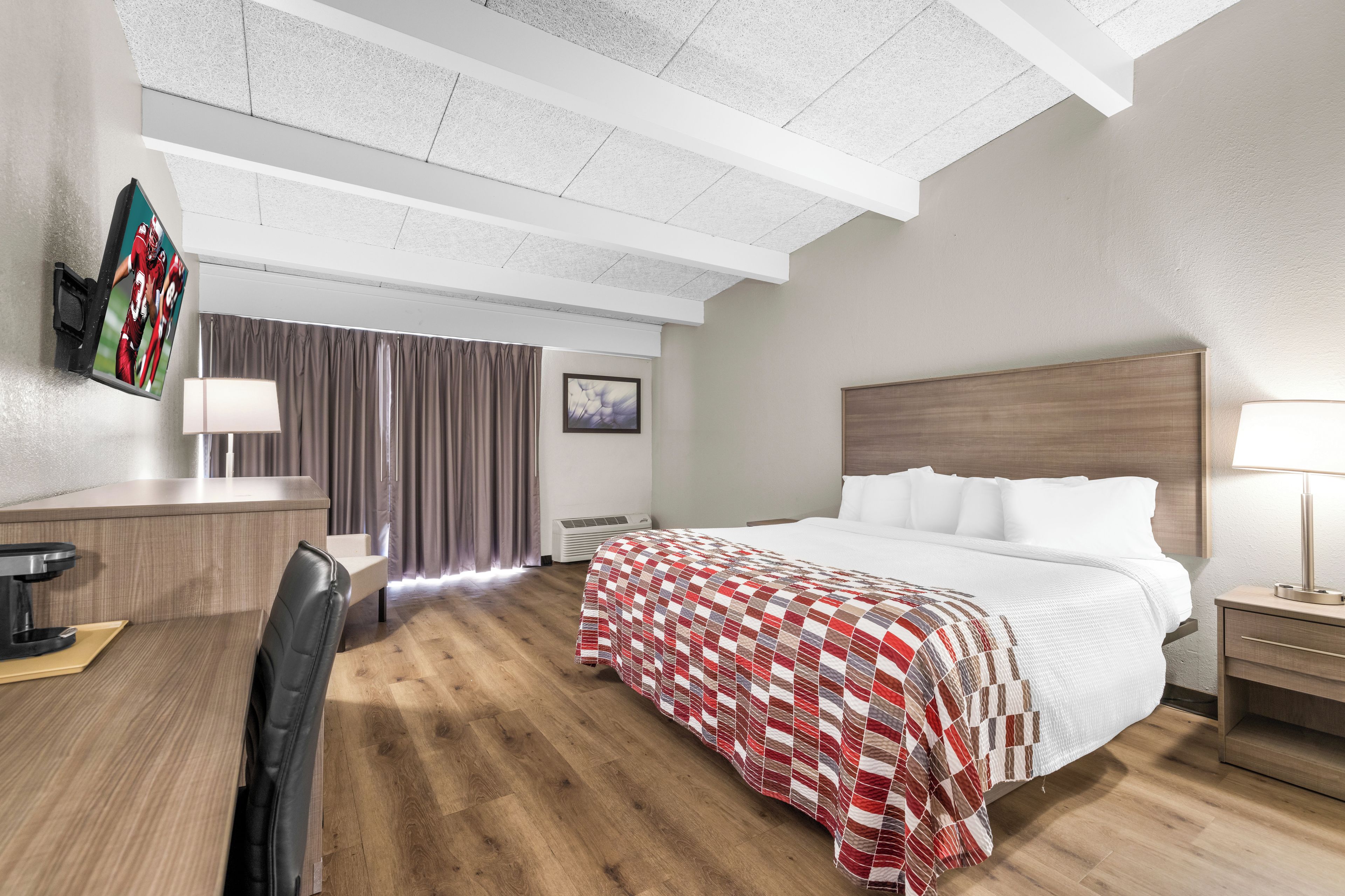A hotel room with a bed, bedside table, desk, chair, and a TV mounted on the wall.