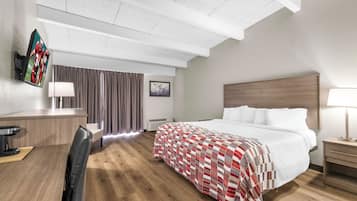 A hotel room with a bed, bedside table, desk, chair, and a TV mounted on the wall.