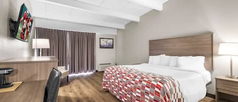 A hotel room with a bed, bedside table, desk, chair, and a TV mounted on the wall.