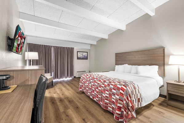 A hotel room with a bed, bedside table, desk, chair, and a TV mounted on the wall.