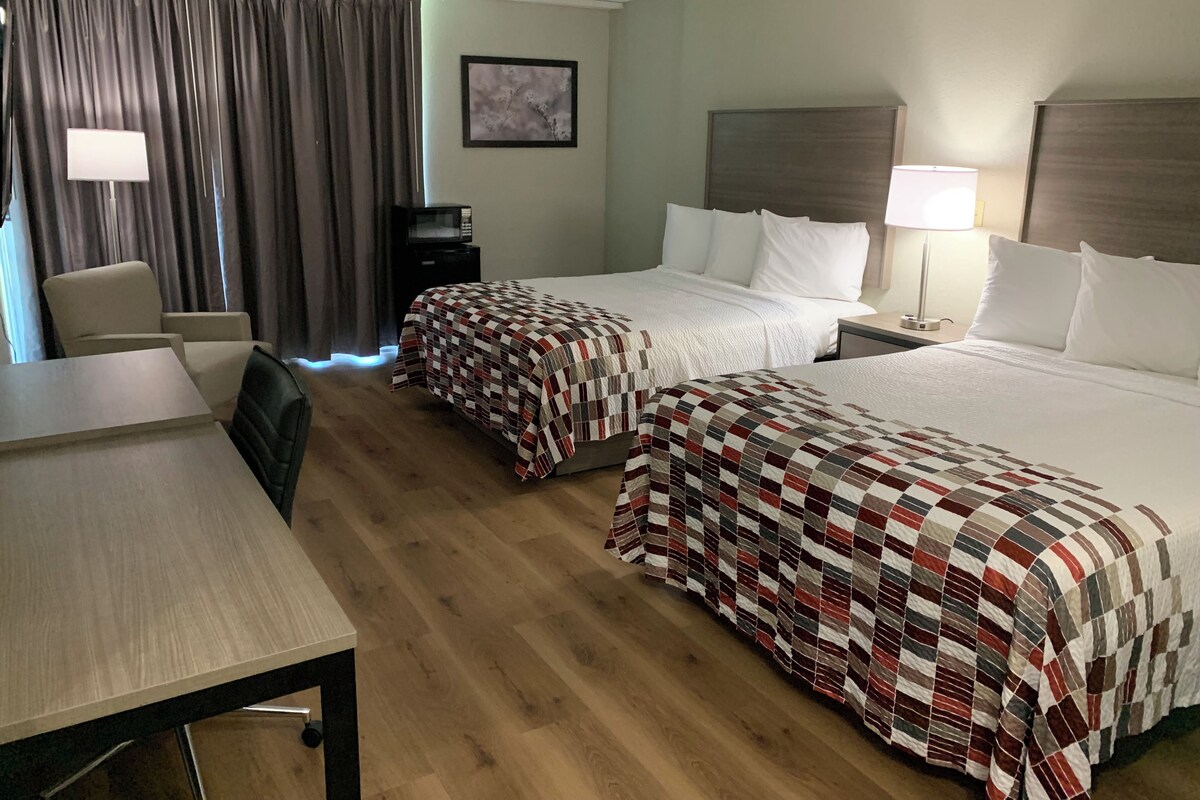 A hotel room with two beds, a desk, a chair, a TV, and a painting on the wall.