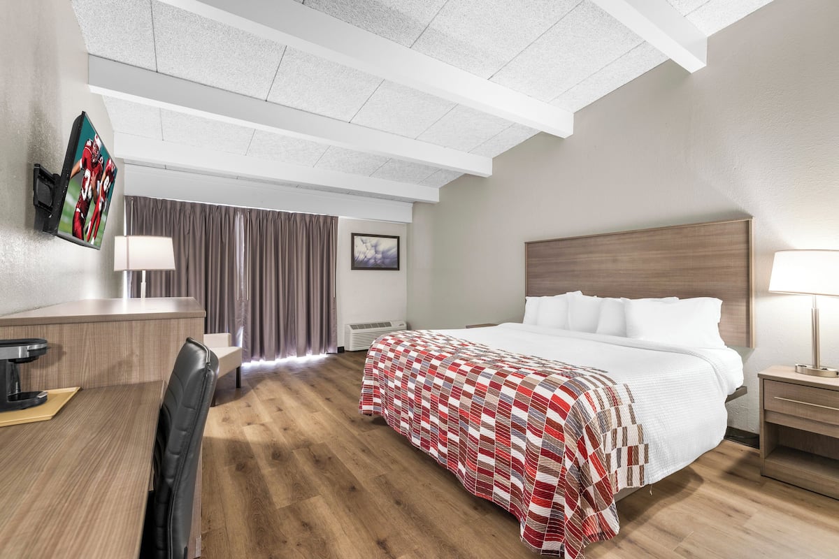 Habitación de hotel con cama, mesitas de noche, escritorio, silla, televisor y ventana con cortinas.