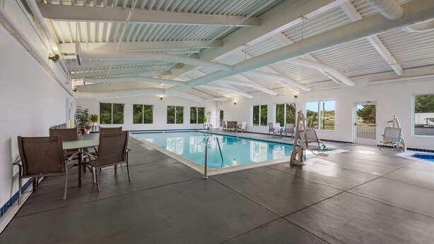 An indoor swimming pool with a high ceiling, large windows, and a dining area with chairs and a table. - Country Inn & Suites by Radisson, Fredericksburg South (I-95), VA (Fredericksburg)