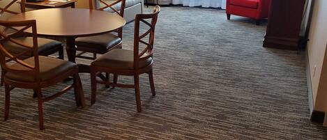 A hotel room with a dining area, a sofa, a red armchair, and a television.