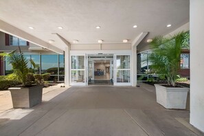 A spacious entrance area with a modern design, featuring a glass door entrance, potted plants, and a concrete floor. - Country Inn & Suites by Radisson, Fredericksburg South (I-95), VA (Fredericksburg)