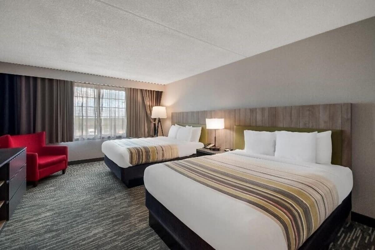 A hotel room with two beds, a red armchair, and a desk.
