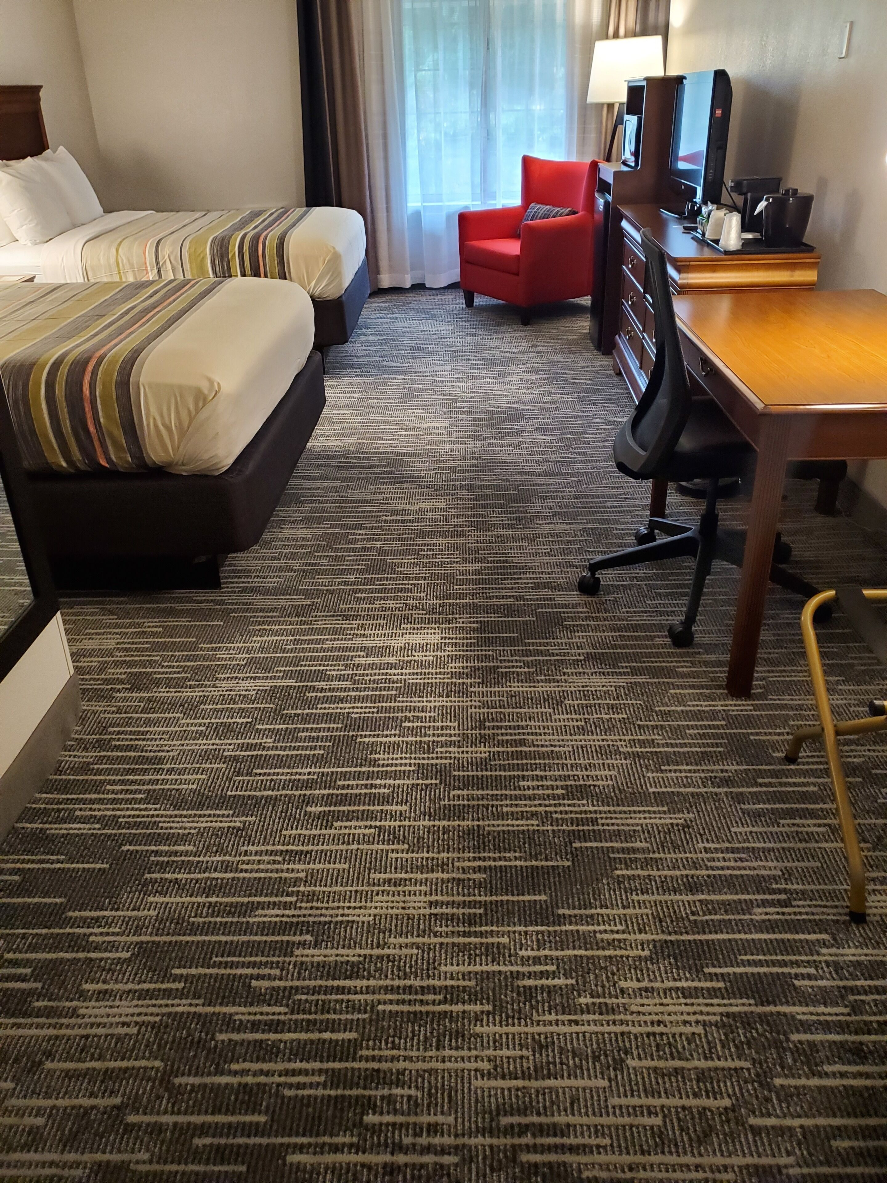 Quarto de hotel com duas camas, uma mesa com computador, uma cadeira e vista para o exterior pela janela.